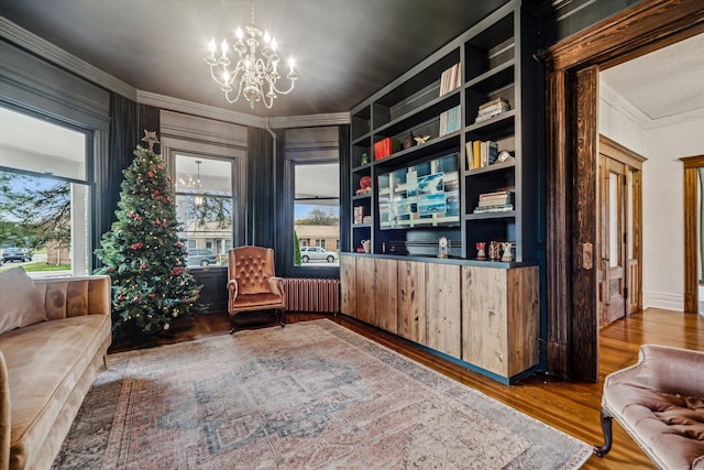 sitting room with built in shelves, ornamental molding, wood-type flooring, and a notable chandelier