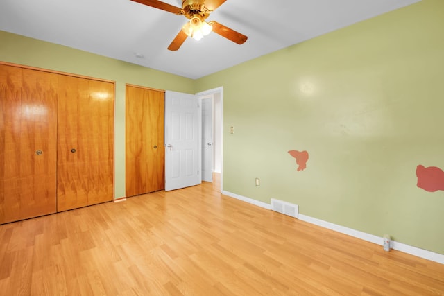 unfurnished bedroom with light wood-type flooring, ceiling fan, and multiple closets