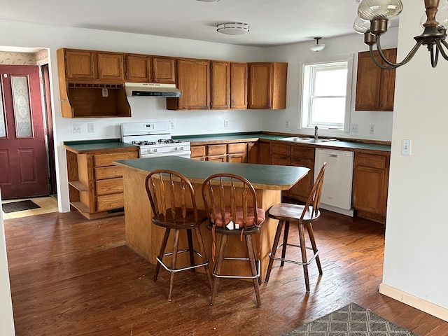 kitchen with white appliances, sink, a kitchen island, dark hardwood / wood-style flooring, and a breakfast bar area