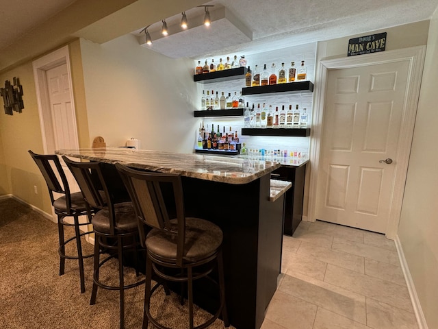 bar featuring a textured ceiling, light stone counters, and light tile patterned flooring