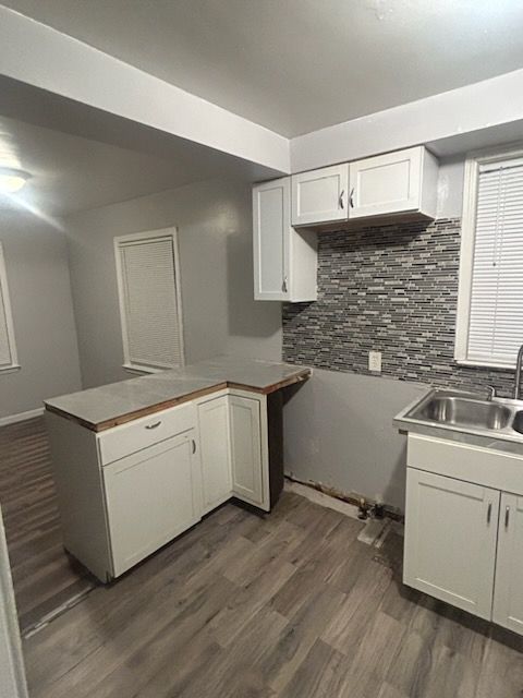 kitchen with decorative backsplash, kitchen peninsula, dark hardwood / wood-style flooring, sink, and white cabinets