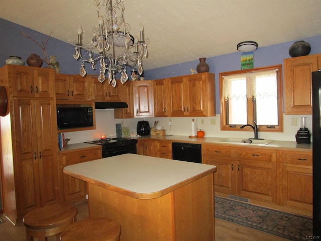 kitchen with light wood-type flooring, black appliances, sink, a notable chandelier, and a center island