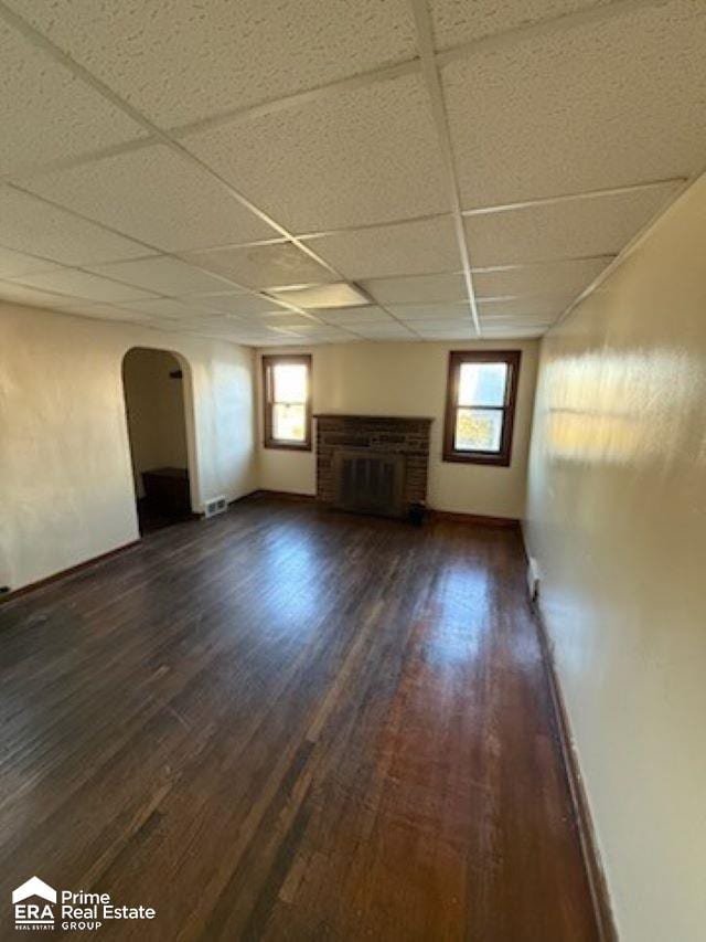 unfurnished living room featuring a paneled ceiling, dark hardwood / wood-style floors, and plenty of natural light