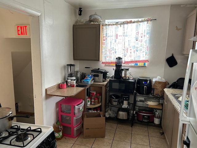 12644 Corbett St, Detroit, MI 48213 - kitchen with white range with gas stovetop, light tile patterned floors, light countertops, and black microwave