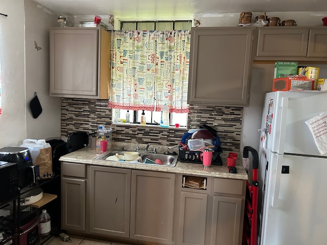 kitchen with gray cabinets, white refrigerator, sink, and backsplash