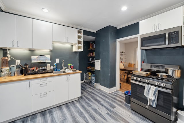 kitchen with white cabinetry, crown molding, light hardwood / wood-style floors, and appliances with stainless steel finishes