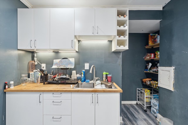 kitchen with dark hardwood / wood-style flooring, white cabinetry, ornamental molding, and sink