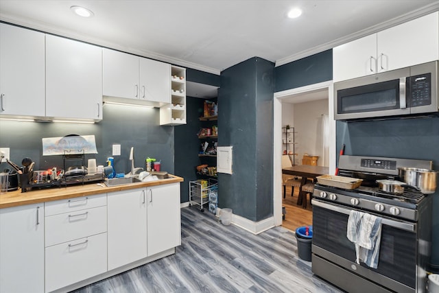 kitchen with light hardwood / wood-style floors, white cabinetry, stainless steel appliances, and ornamental molding