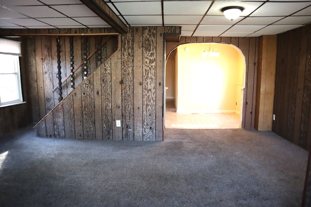 unfurnished room featuring a drop ceiling, wood walls, and carpet floors