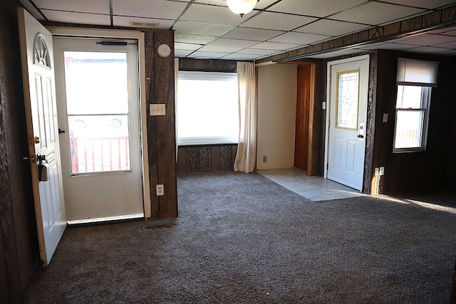 carpeted foyer featuring a paneled ceiling, a wealth of natural light, and wooden walls