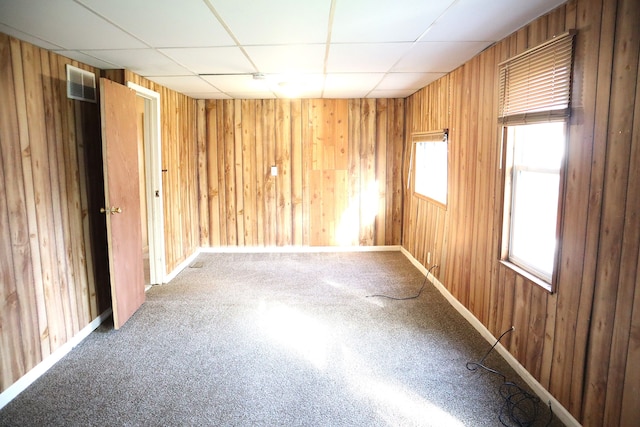 carpeted spare room featuring a paneled ceiling, wood walls, and a wealth of natural light