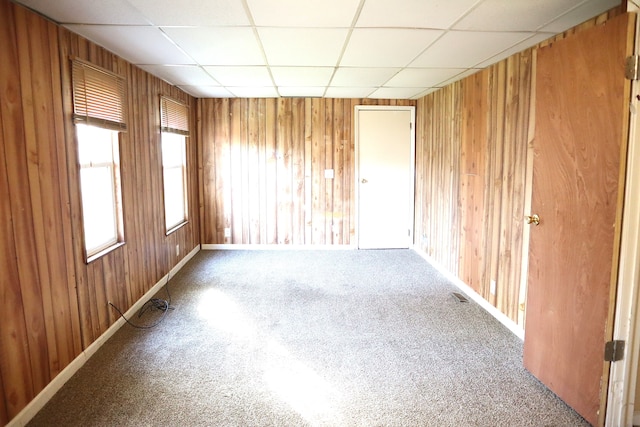 carpeted spare room with a drop ceiling and wood walls