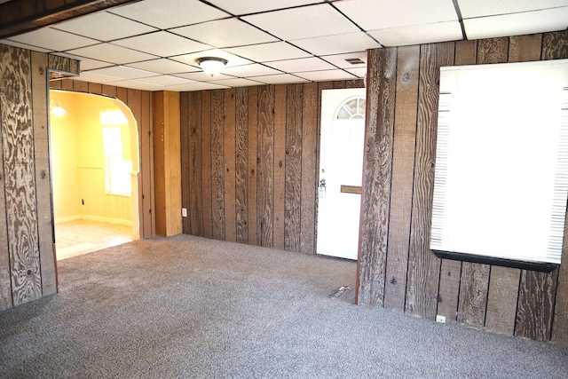 spare room with a paneled ceiling, wooden walls, and carpet