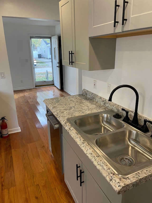 kitchen with light stone countertops, sink, light hardwood / wood-style flooring, stainless steel dishwasher, and white cabinets