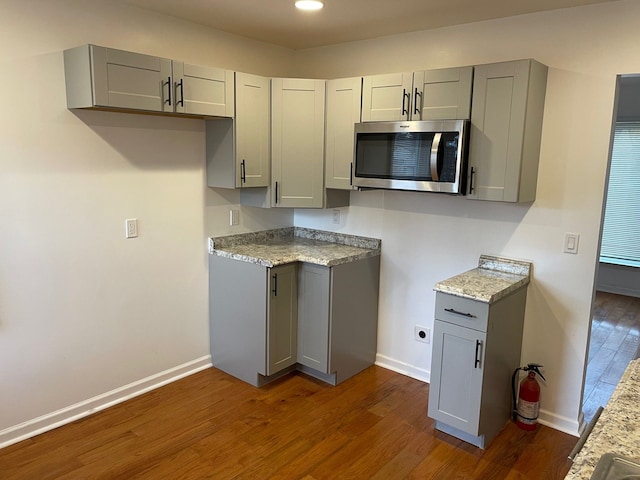 kitchen with gray cabinets, dark hardwood / wood-style flooring, and light stone countertops