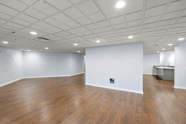 basement featuring a paneled ceiling, sink, and dark hardwood / wood-style floors