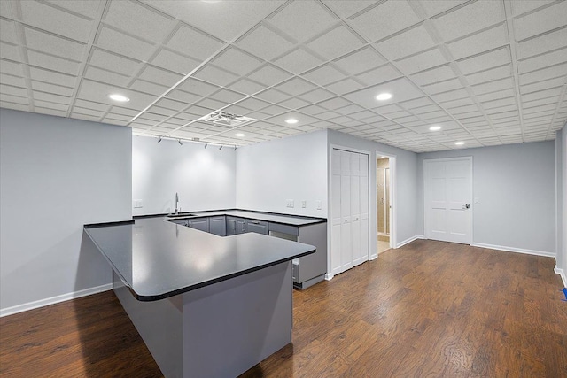 kitchen with a drop ceiling, sink, gray cabinets, dark hardwood / wood-style flooring, and kitchen peninsula