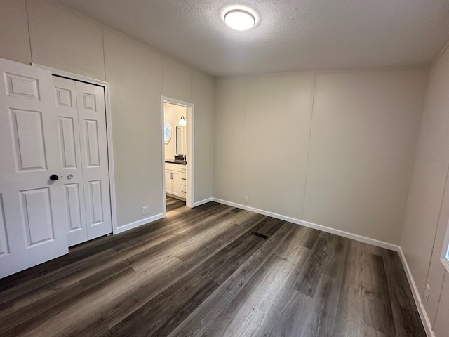 unfurnished bedroom with a textured ceiling, dark hardwood / wood-style flooring, ensuite bathroom, and a closet