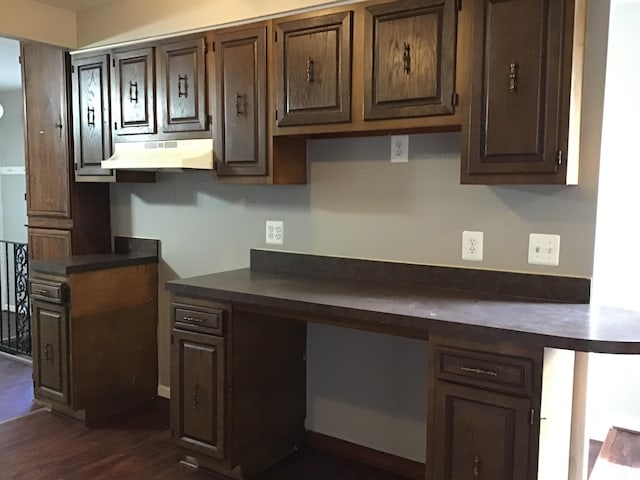 kitchen with dark brown cabinetry, dark hardwood / wood-style flooring, built in desk, and ventilation hood