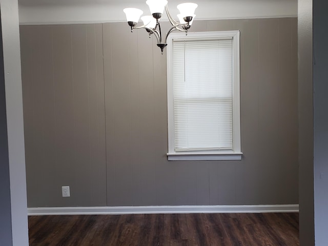 empty room featuring dark hardwood / wood-style floors, an inviting chandelier, wooden walls, and crown molding