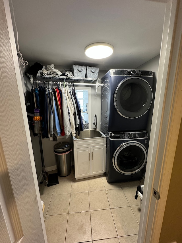 laundry area featuring sink, light tile patterned floors, cabinets, and stacked washer and clothes dryer