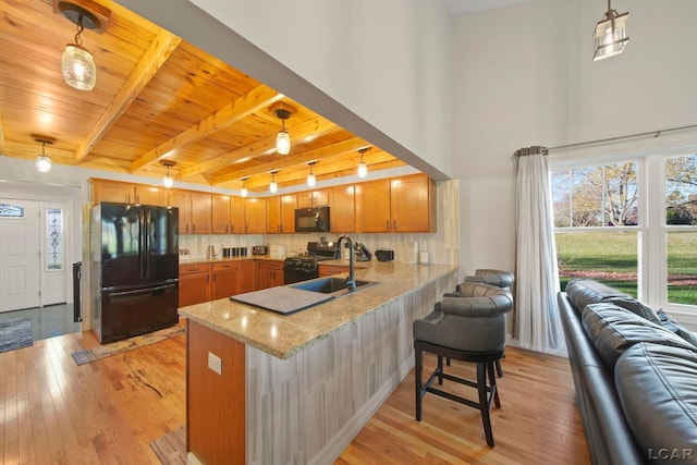 kitchen with black appliances, pendant lighting, backsplash, and light hardwood / wood-style flooring