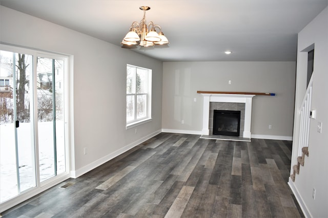 unfurnished living room with a tiled fireplace, dark wood-type flooring, and a chandelier