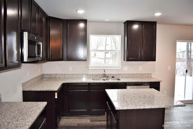 kitchen with sink, dark brown cabinets, stainless steel appliances, dark hardwood / wood-style floors, and light stone counters
