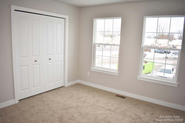unfurnished bedroom featuring multiple windows, light colored carpet, and a closet