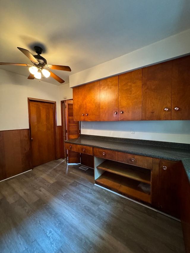 kitchen with wood walls, dark hardwood / wood-style floors, ceiling fan, and built in desk