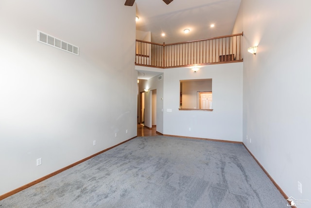 unfurnished living room with ceiling fan, carpet flooring, and a high ceiling