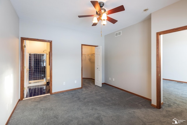 unfurnished bedroom with ceiling fan, dark carpet, ensuite bathroom, and a walk in closet