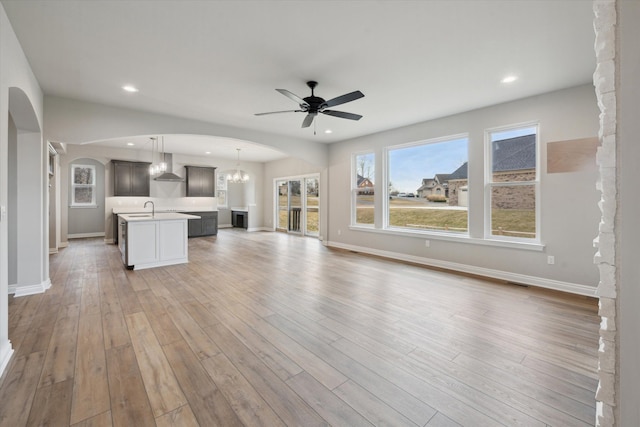 unfurnished living room featuring visible vents, recessed lighting, ceiling fan with notable chandelier, light wood-style flooring, and arched walkways