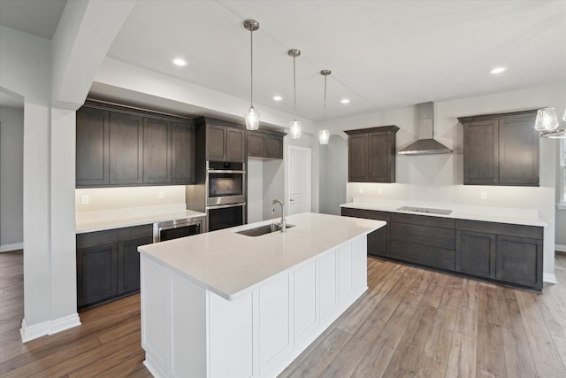 kitchen featuring stainless steel double oven, a sink, dark brown cabinetry, wall chimney range hood, and light wood-type flooring