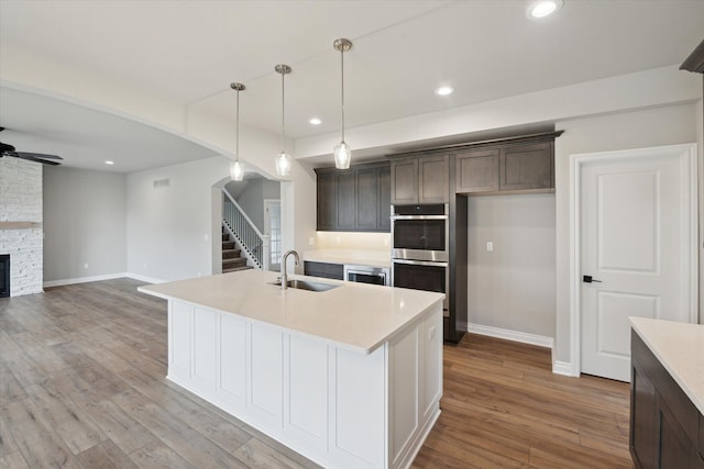 kitchen with ceiling fan, double oven, recessed lighting, wood finished floors, and a sink