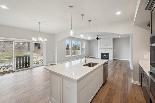 kitchen featuring open floor plan, dishwasher, ceiling fan with notable chandelier, a fireplace, and a sink