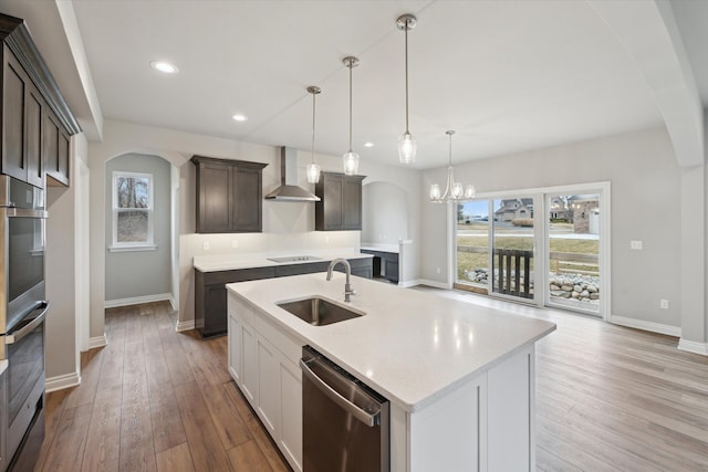 kitchen featuring appliances with stainless steel finishes, wood finished floors, arched walkways, wall chimney exhaust hood, and a sink