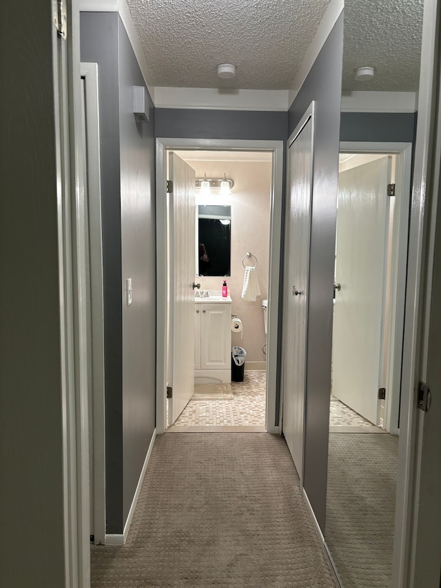 hallway with sink, light colored carpet, and a textured ceiling