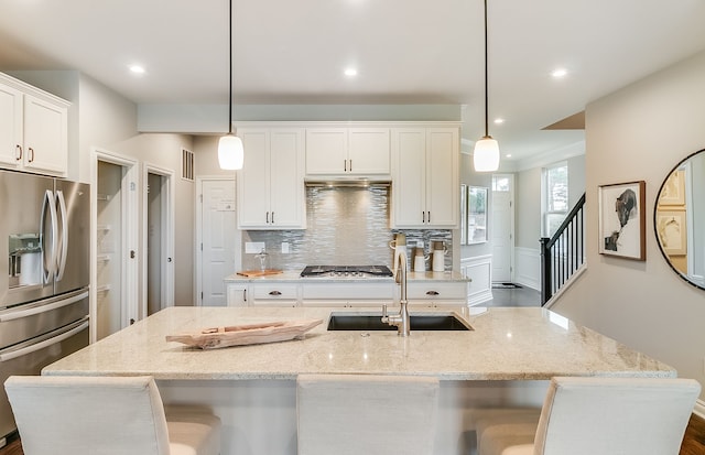 kitchen with stainless steel appliances, light stone countertops, an island with sink, white cabinets, and decorative light fixtures