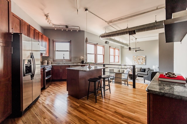 kitchen featuring appliances with stainless steel finishes, a kitchen breakfast bar, hardwood / wood-style flooring, dark stone countertops, and a center island