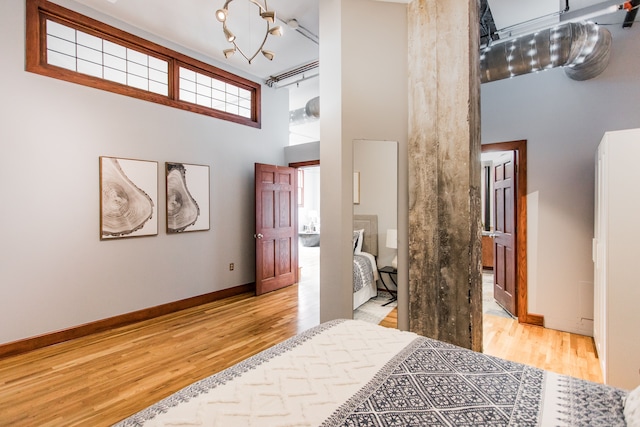 bedroom featuring an inviting chandelier, a towering ceiling, rail lighting, and light wood-type flooring