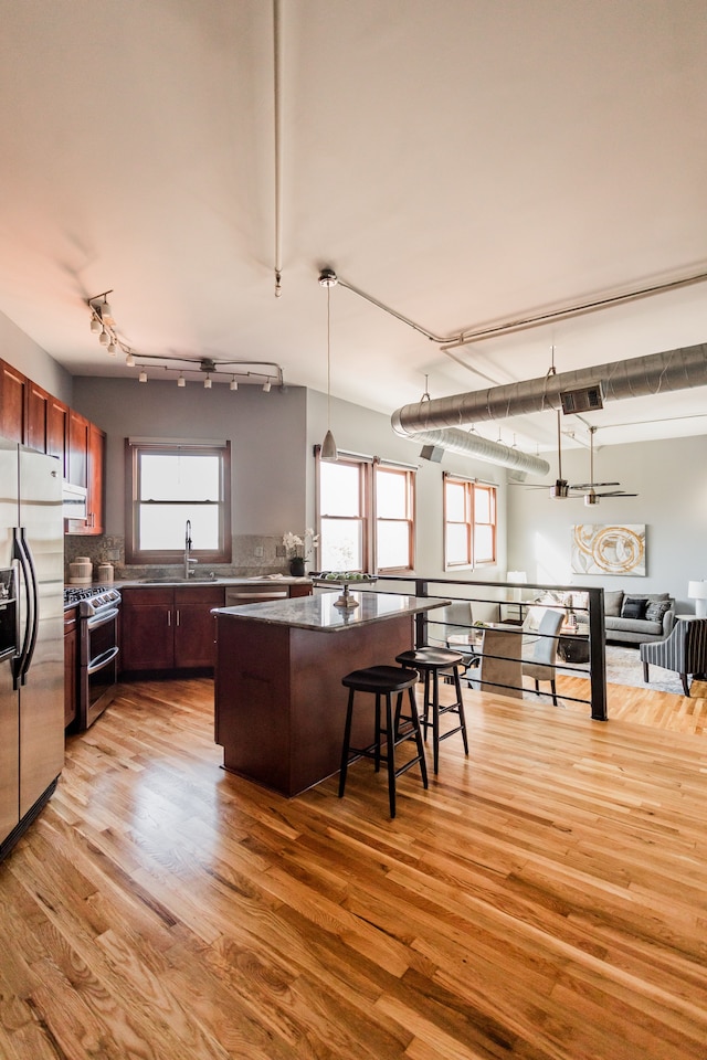 kitchen featuring light hardwood / wood-style flooring, a breakfast bar area, appliances with stainless steel finishes, hanging light fixtures, and a center island