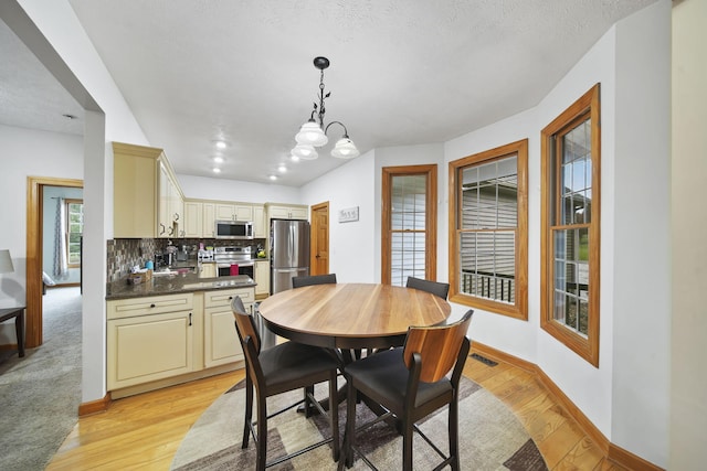 dining space with light hardwood / wood-style floors, a textured ceiling, and an inviting chandelier