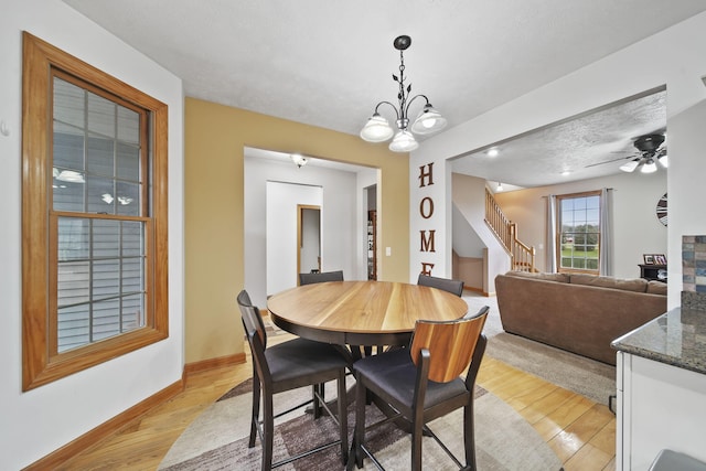 dining room with ceiling fan with notable chandelier, a textured ceiling, and light hardwood / wood-style flooring