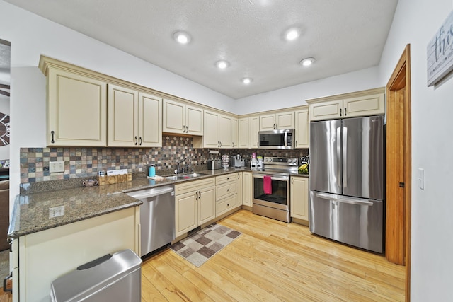 kitchen with decorative backsplash, light hardwood / wood-style flooring, cream cabinetry, and appliances with stainless steel finishes