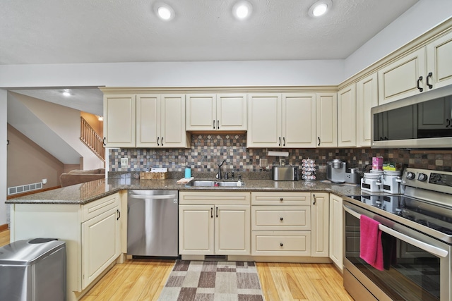 kitchen with decorative backsplash, kitchen peninsula, stainless steel appliances, light hardwood / wood-style flooring, and cream cabinetry