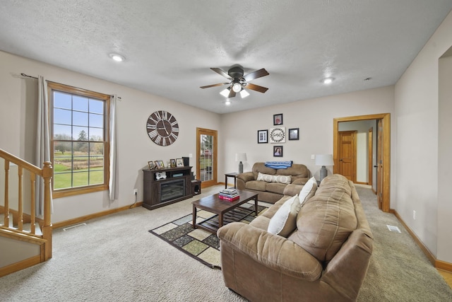 living room with ceiling fan, a fireplace, light colored carpet, and a textured ceiling