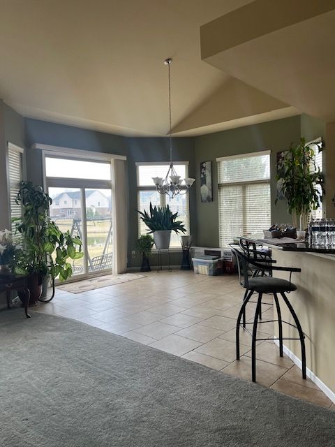 22031 Goldenwillow Dr, Macomb, MI 48044 - dining space featuring light tile patterned flooring, a notable chandelier, vaulted ceiling, and a healthy amount of sunlight