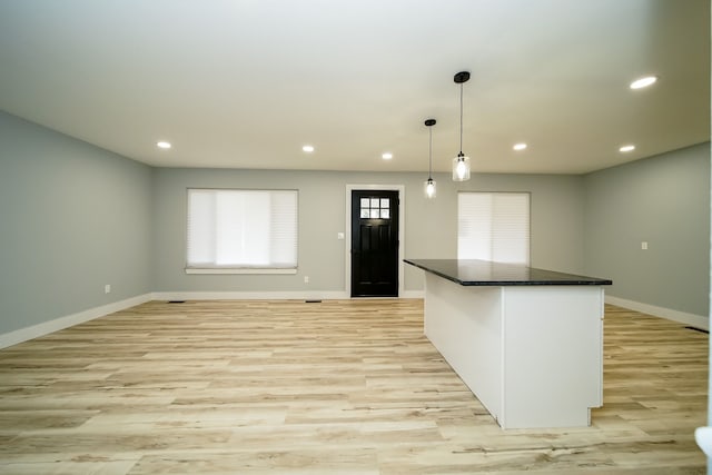 kitchen featuring a center island, white cabinets, hanging light fixtures, dark stone countertops, and light hardwood / wood-style floors