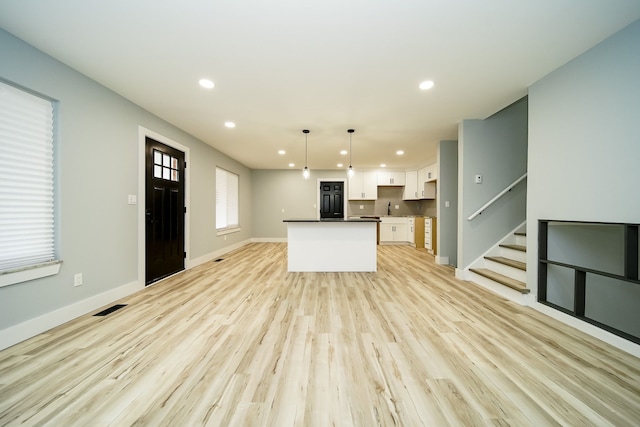 kitchen with white cabinetry, sink, a center island, pendant lighting, and light wood-type flooring